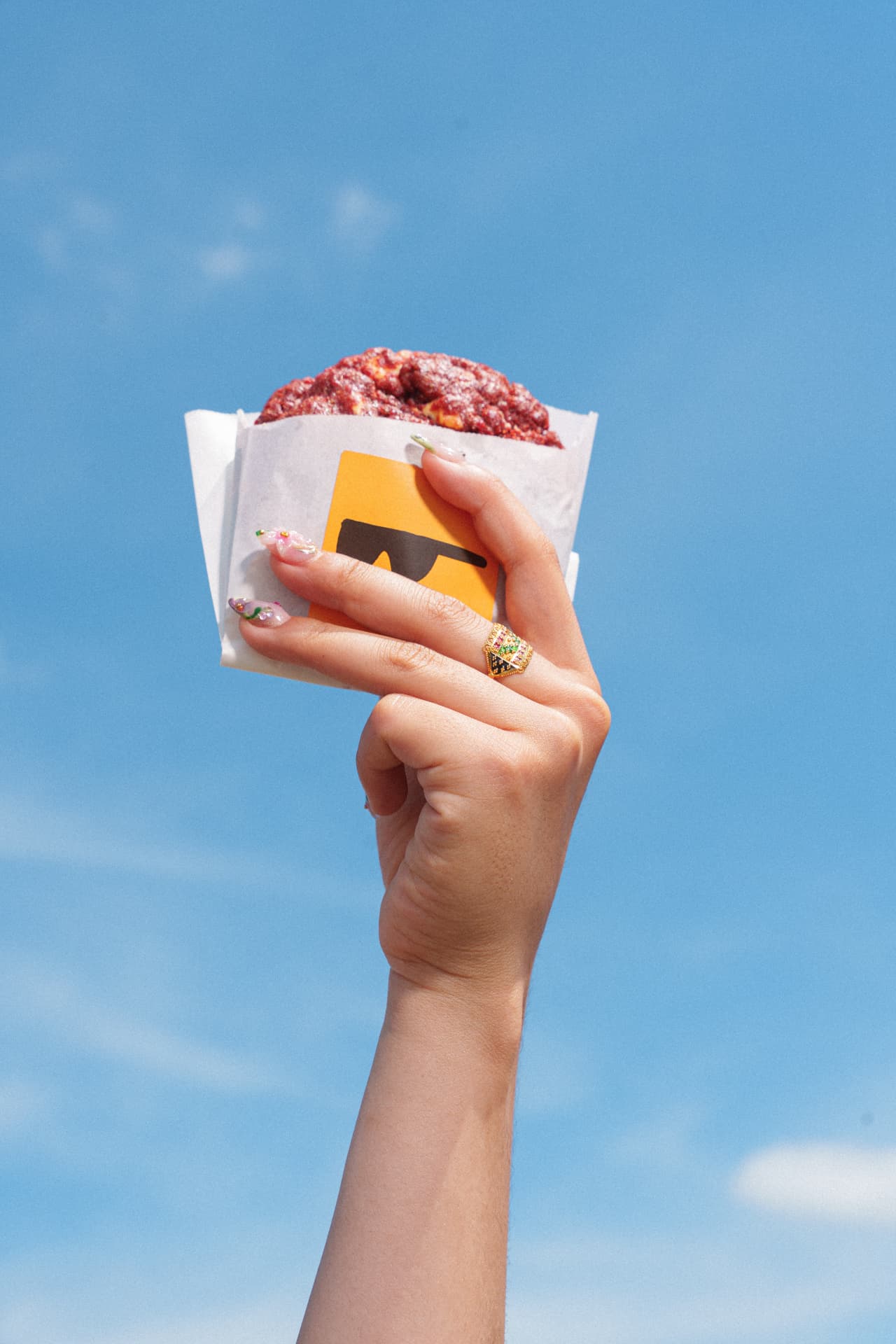 Hand holding a red velvet Daily Cookie against the sky