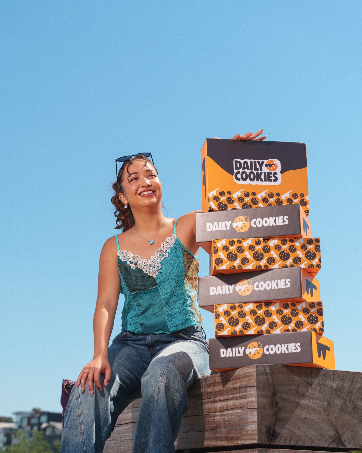 Woman sitting next to a tall stack of Daily Cookies boxes under a blue sky